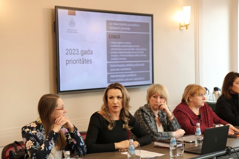 Inese Šteina preznetē 2023.gad prioritātes pie galda kopā ar TM padotības iestāžu vadītājiem, aiz muguras ekrāns ar prezentāciju.