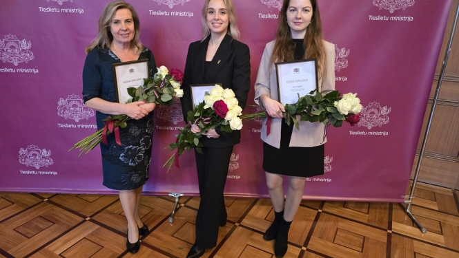 Apbalvojuma saņēmējas pie ministrijas banera