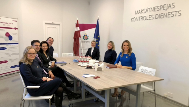 Pie sarunu galda sēž astoņi smaidīgi cilvēki